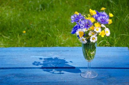 wild summer flowers in wineglass on blue old table in gardenの写真素材