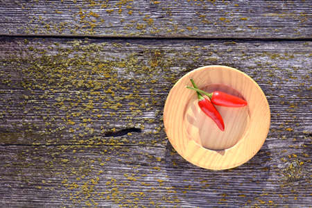 Two red ripe hot chili peppers in wooden plate on old plank background  の写真素材