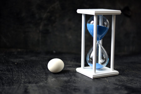 Still-life nature morte with white egg and sandglass on black background  
