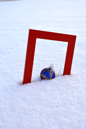 Red picture frame and Christmas bauble on fresh snowの写真素材