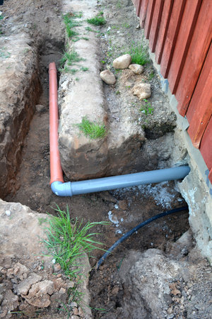 Trench near wooden village house with water and sewerage pipes