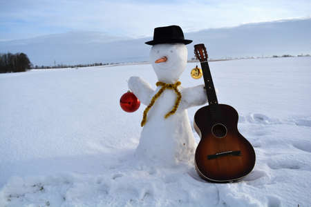 Christmas new year snowman on field with baubles, hat and old guitarの写真素材