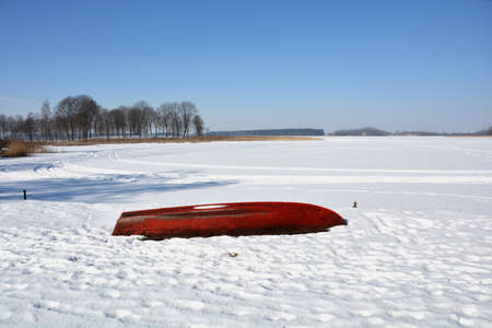 Red old boat on snowy winter lake coast, winter landscapeの写真素材