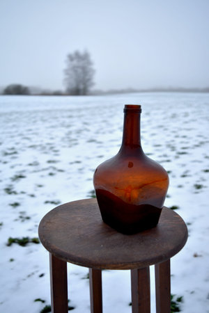 Winter still life on snowy field with table and old ancient brown bottle