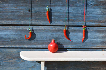 Red chili peppers hanging on wooden wall and pomegranate on white shelfの写真素材