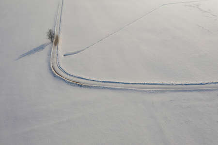 aerial view over snowy field and road with lonely treeの写真素材