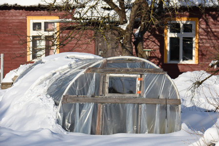 Winter time greenhouse near farm house on snowの写真素材