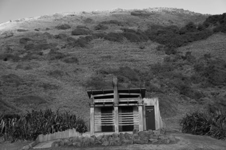 A wooden restroom with a hill behind it.  Taken at Hamilton gap beach, In Auckland, New Zealand.の写真素材