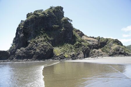 A view of Lion's rock at Phia beach in Auckland, New Zealand.  View of the land, sea, sand and sky.の写真素材