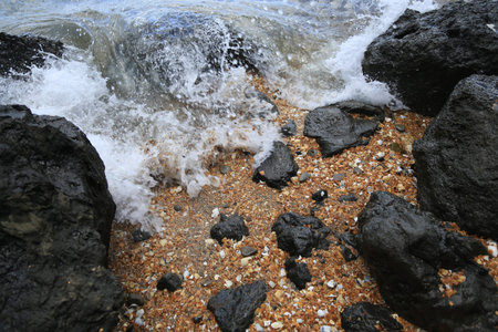 A wave crashing on large and small rocks on a beach.  Taken on Red Beach in Auckland, New Zealand.