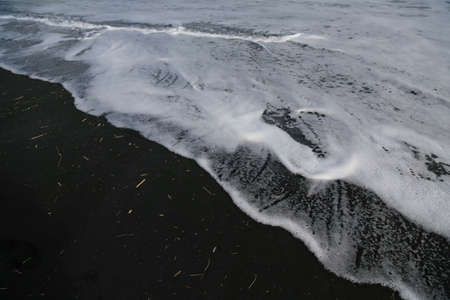 The foam from the waves on black sand.  Taken on Port Waikato beach in New Zealand.の写真素材