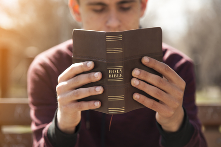 Young man holding and reading holy bible outdoorsの写真素材