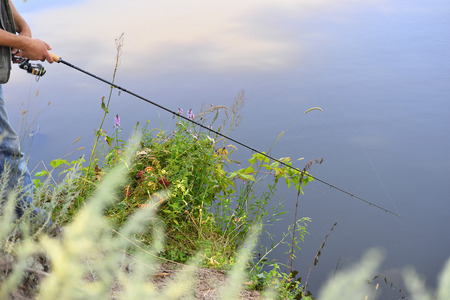 Fishing in river. A fisherman with a fishing rod on the river bank. Man fisherman catches a fish.  The concept of a rural getaway. Article about fishing.の写真素材