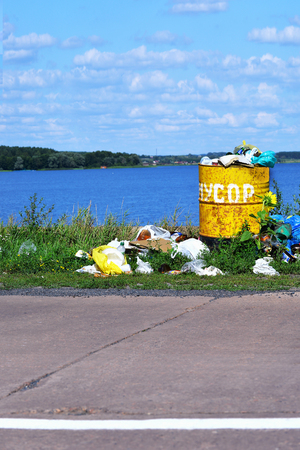 Overflowing barrel with household waste and waste disposal on the waterfrontの写真素材