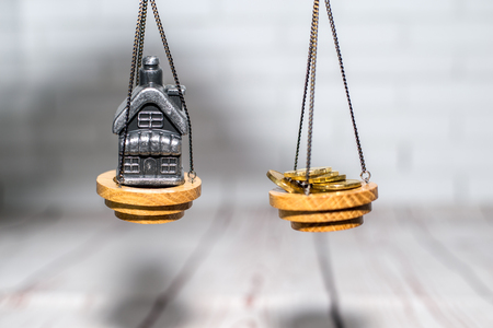 Stack of coins and a small house on the scales. The concept of choice, cash savings and purchase of real estateの写真素材