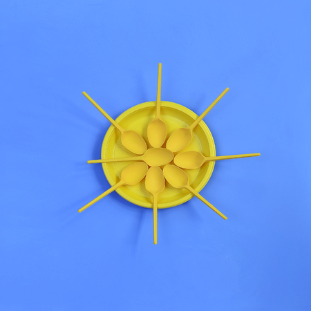 A yellow plastic plate and spoons lay around it on a bright blue background. The concept of a holiday, picnicの写真素材