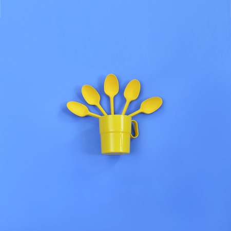 A yellow plastic mug and spoons lay in it on a bright blue background. The concept of a holiday, a picnicの写真素材