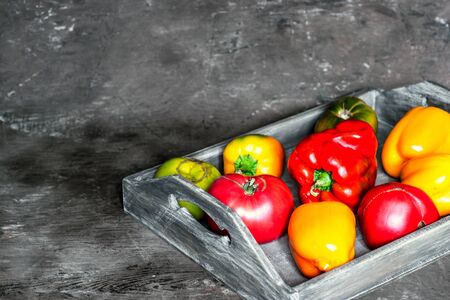 Imperfect natural peppers and tomatoes on an old wooden tray on a dark background. Healthy eating concept. Copy Space.の写真素材