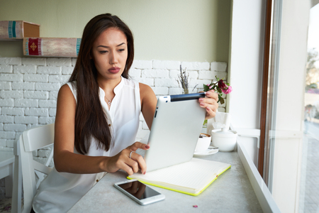 Young happy hipster girl speaking with her friend by mobile phone while relaxing in cozy coffee shop, charming lady with beautiful smile talking on cell telephone while sitting in caの写真素材