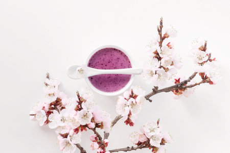 Blueberry smoothie with spoon on white background decorated with blossoming apricot branch. Flat lay, top view, copy space.の写真素材