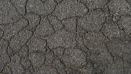 Asphalt background texture with cracks. Close-up image of cracked asphalt