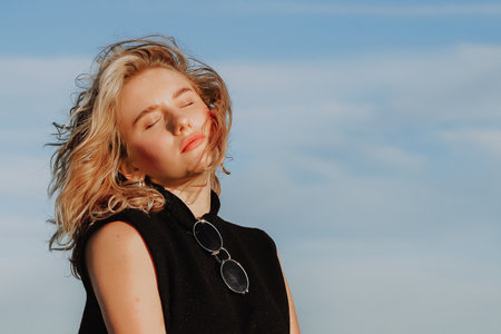 Young blond woman with closed eyes enjoying sunlight outdoors. Concept of relaxation, well-being, and summerの写真素材