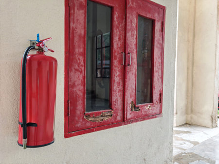 Wall-mounted fire extinguisher beside aged fire hose cabinet with chipped paint and glass panels