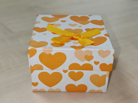 White gift box with orange hearts and yellow ribbon, placed on wooden surface
