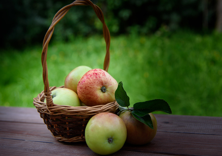 Juicy apples in a basket on a wooden table on a green backgroundの写真素材
