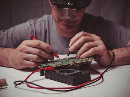 A male engineer is repairing an electronic board. Measurement of parameters and soldering of the electronic board.の写真素材