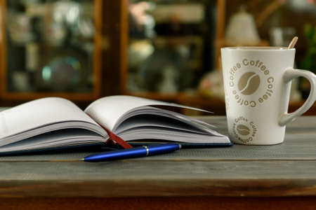 Open notebook with pen and coffee mug on a wooden table.