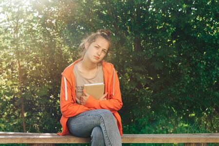 Cute girl with a book in her hands on a sunny summer day sits in a park.の写真素材
