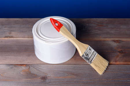 A can of white paint and a paintbrush on a wooden table.の写真素材