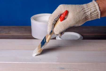 Painting the board with white paint. A can of paint and a brush on a wooden table.の写真素材