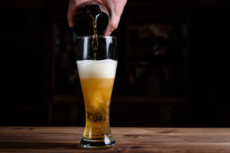 Glass with beer on a wooden table. Beer is poured into a glass from a bottle.