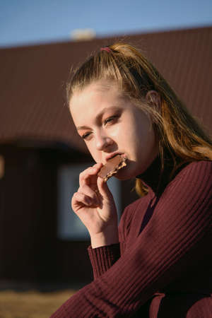 A young girl is thoughtful and eats chocolate in nature.の写真素材