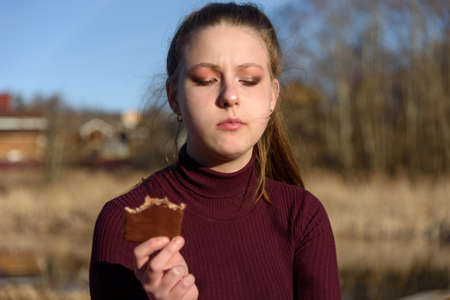 A young girl is thoughtful and eats chocolate in nature.の写真素材