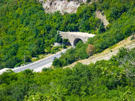 View from the high green hills on the serpentine highway and a mountain tunnel lined with stoneの写真素材