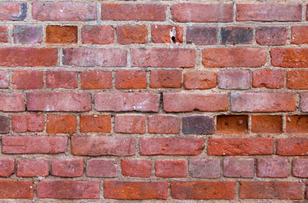 Close-up background of ancient red brick wall shabby aged with grains of stone dips and scuffsの写真素材