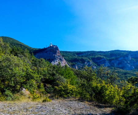 View from below from a rocky platform at a rest stop on a hike at the church on the mountain against the sunny skyの写真素材