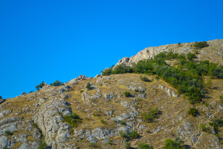 Path along the mountain to the top among bushes and stones against the blue sky in a hot southern countryの写真素材