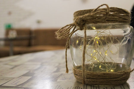 jar lantern with a glowing garland decor on a table in the interior of a cafe on a blurred background in natural colorsの写真素材
