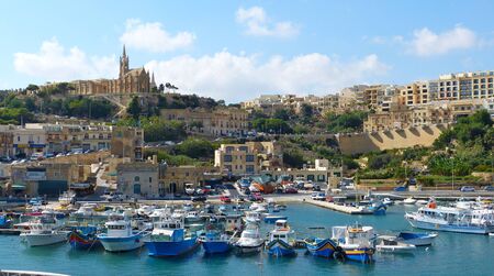 Mgarr, Malta - September 27, 2013. View over Mgarr harbour on Gozo island, with residential and commercial buildings, church on top of the hill and boats.のeditorial素材