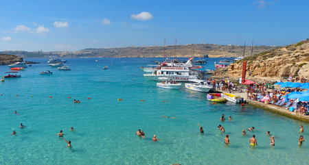 Comino, Malta - September 28, 2013. View of the Blue Lagoon on Comino island of Malta, with people, cruise boats and Gozo island in the background. The incredibly beautiful and inviting Blue Lagoon is the biggest attraction of Comino. It is a sheltered coのeditorial素材
