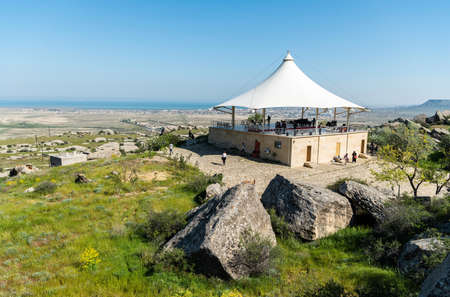 Gobustan, Azerbaijan - May 1, 2019. Landscape in Gobustan national park, with pavilion, people and Gobustan settlement in the distance.のeditorial素材