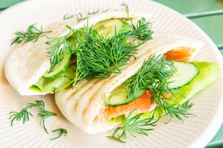 Pita sandwich with smoked salmon, cucumber, lettuce and chopped dill on top.の写真素材