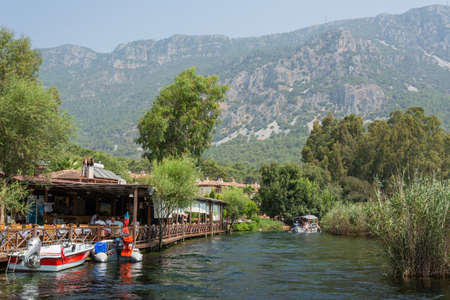 Akyaka, Mugla, Turkey - July 30, 2016. Azmak stream in Akyaka village in Mugla province of Turkey, with restaurant, boats and Sakar mountains in the background.のeditorial素材