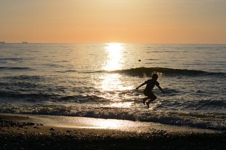 Boy jumping in the waves of the sea at sunsetの写真素材