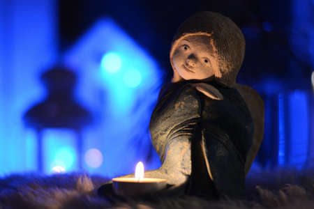A ceramic candlestick in the shape of an angel stands on the table in the Christmas lights of garlandsの写真素材