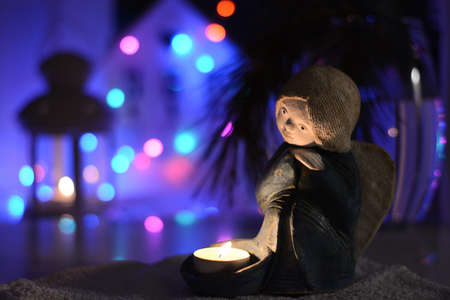 A ceramic candlestick in the shape of an angel stands on the table in the Christmas lights of garlandsの写真素材